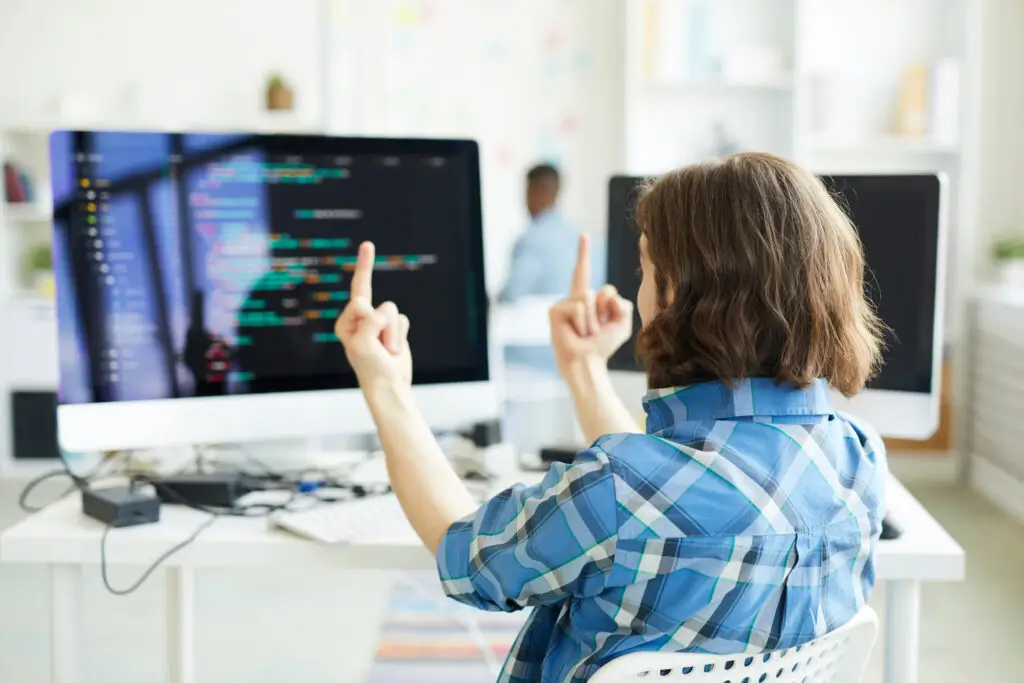 Genervter Entwickler zeigt zwei Bildschirmen mit JavaScript-Code den Mittelfinger – Frust über komplexe Webentwicklung.