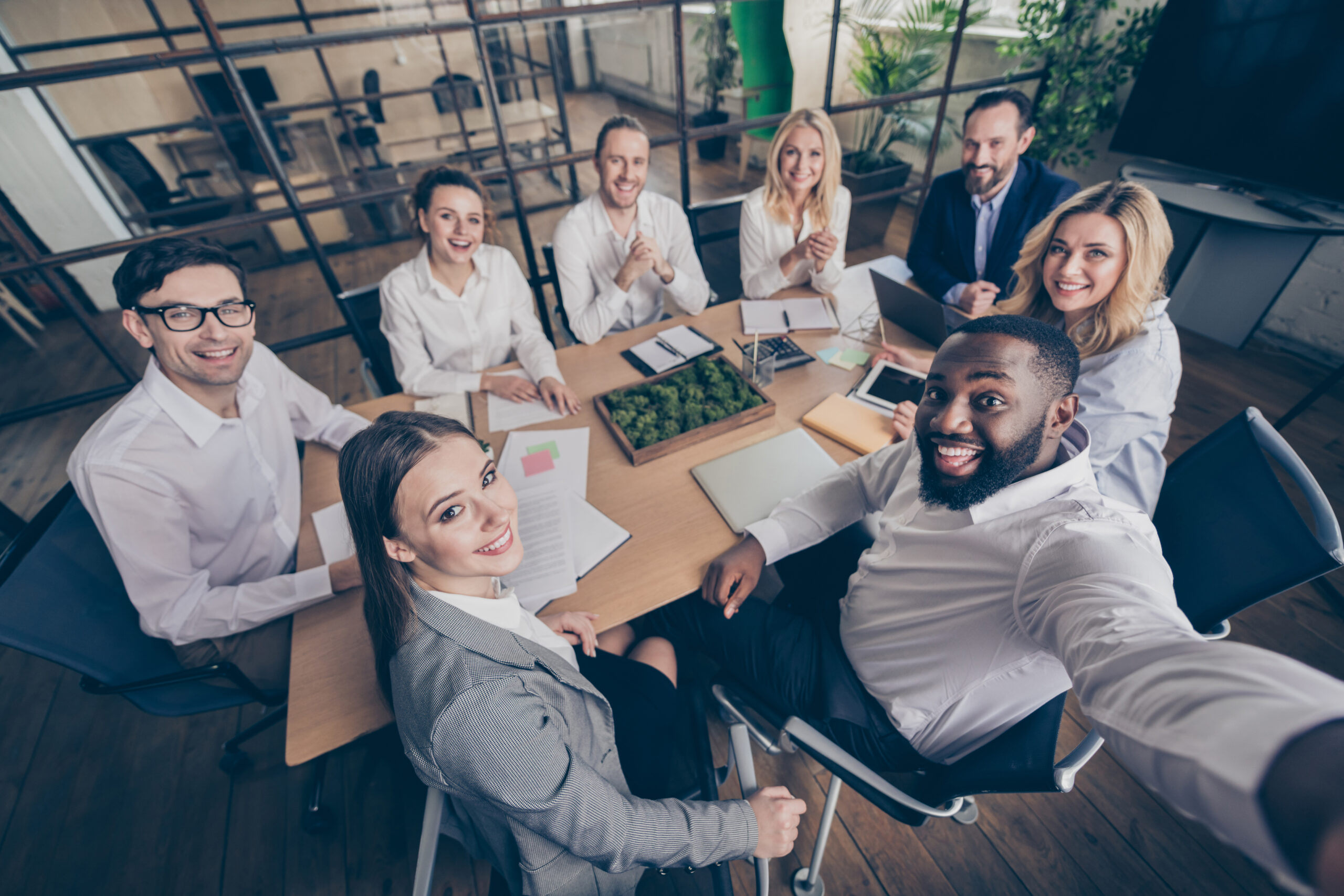 Diverse Gruppe von Kollegen sitzt lächelnd an einem Konferenztisch in einem modernen Büro und blickt gemeinsam in die Kamera.