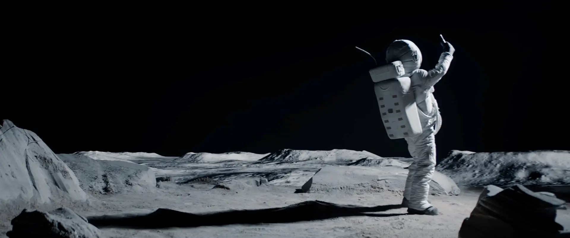 Astronaut auf einer kargen Mondlandschaft mit erhobenem Arm vor tiefschwarzem Himmel.